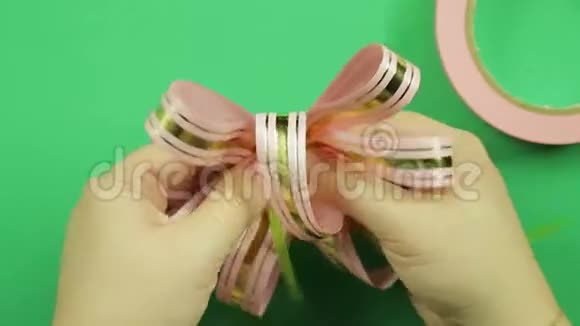女性的双手在绿色背景上形成粉红色丝带蝴蝶结视频的预览图