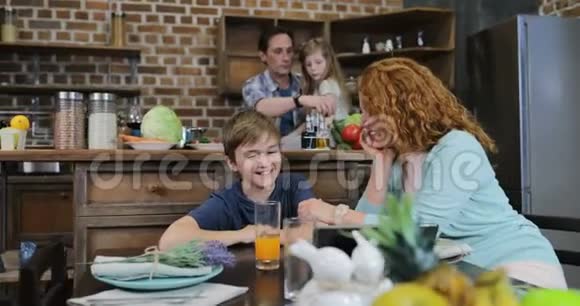 母亲和儿子用平板电脑说话父亲和女儿在厨房做饭家庭幸福视频的预览图