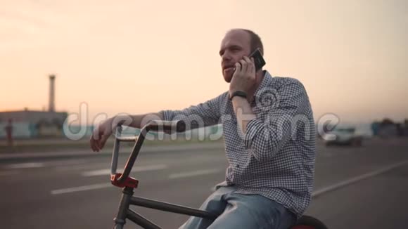 带着bmx自行车的年轻人在街上日落时使用他的手机慢动作视频的预览图
