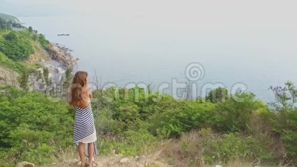 在多云的天空下无人机从站在山顶的女孩身上移开视频的预览图