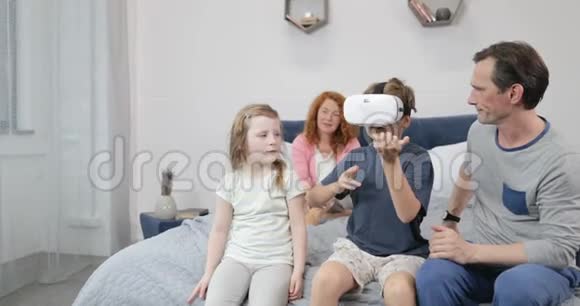 家庭在卧室里看穿虚拟现实眼镜的儿子游戏父母和孩子一起度过早晨视频的预览图