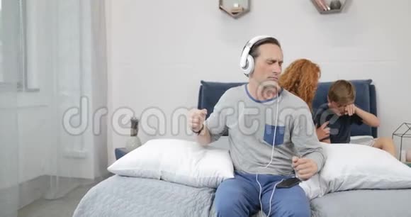 快乐的父亲在卧室里用新耳机听音乐而不是与儿子交流视频的预览图