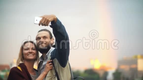 年轻的幸福夫妇在夕阳下散步拍自拍照片微笑的男人和女人使用智能手机视频的预览图