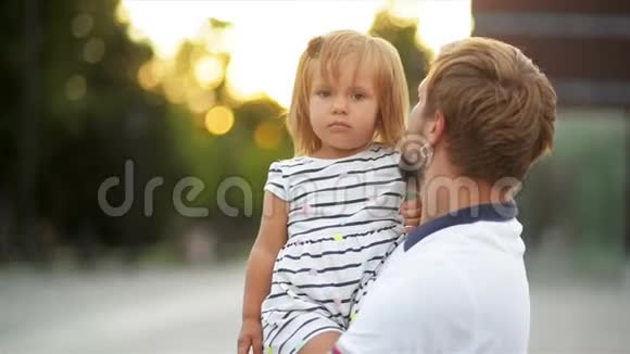 小可爱的女孩坐在父亲的手上在城市日落时和父亲在户外交谈视频的预览图