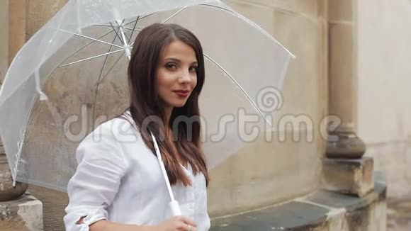 年轻女孩的画像手里拿着伞站在街上看着镜头视频的预览图