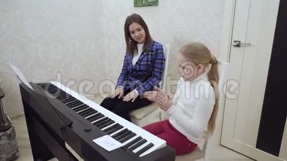 年轻的老师和小可爱的女孩在电动钢琴上演奏视频的预览图