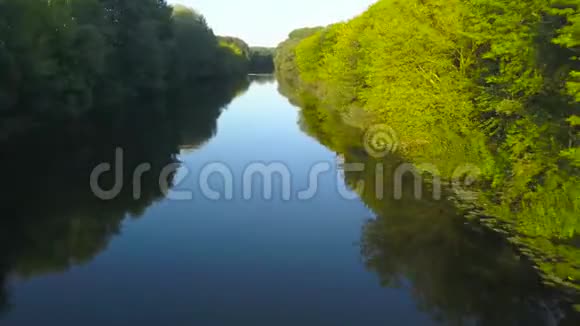 日落时分飞过一条被绿树环绕的宁静的河流视频的预览图