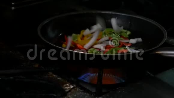 专业厨师兼消防用明火在黑暗的背景下烹饪蔬菜和食物视频的预览图