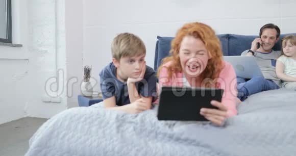 一家人一起在卧室里度过一个早晨母亲和儿子一起看视频嘲笑父亲在打电话视频的预览图