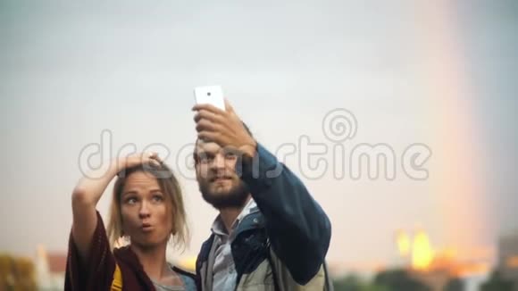 年轻夫妇在背景上拍摄彩虹自拍照片开朗的男人和女人使用智能手机技术视频的预览图
