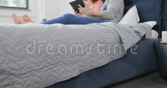 使用数码平板电脑拥抱男人和女人在卧室里聊天浏览互联网视频的预览图