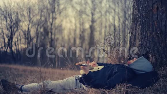 日落时分一个男人躺在橡树下弹吉他视频的预览图
