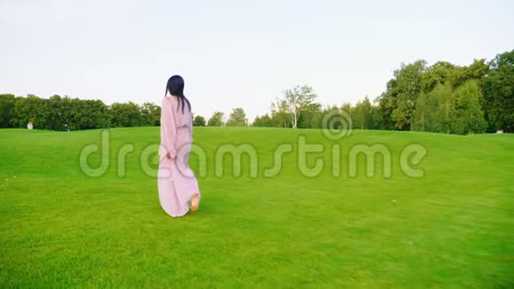 穿着淡粉色裙子的孕妇穿过绿色的草地视频的预览图