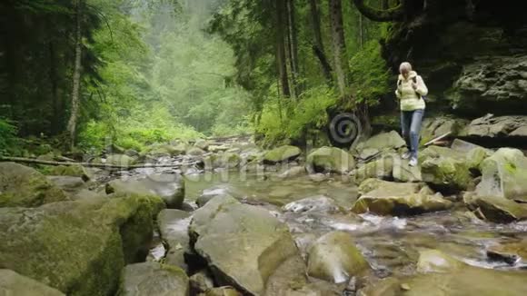 一个背着背包的女游客穿过森林里的一条山河冒险和积极的生活方式视频的预览图