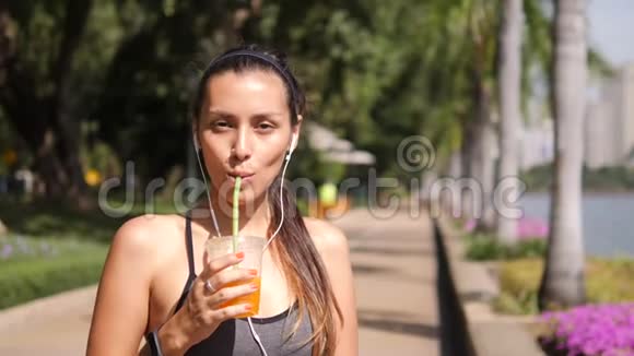 迷人的混合种族瑜伽女孩喝新鲜橙汁后在城市公园4K慢动作泰国视频的预览图
