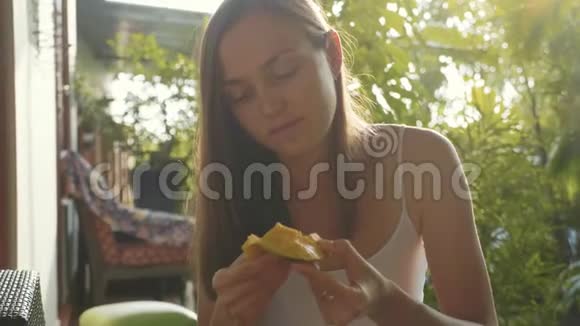 幸福的年轻女子在绿色花园里愉快地吃芒果的肖像视频的预览图