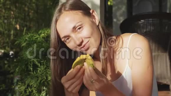 幸福的年轻女子在绿色花园里愉快地吃芒果的肖像视频的预览图