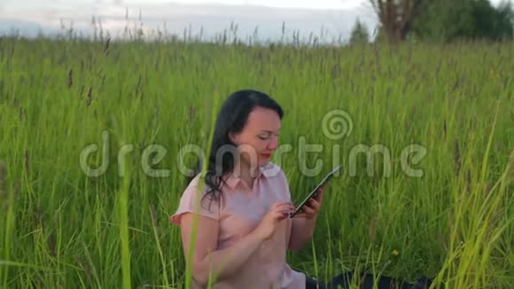 微笑的女人坐在绿草中在公园里的平板电脑上工作镜头移向小车视频的预览图