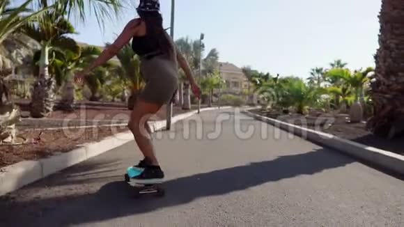 美丽的年轻女孩骑在靠近海滩的道路上棕榈树在长板上缓慢地运动视频的预览图