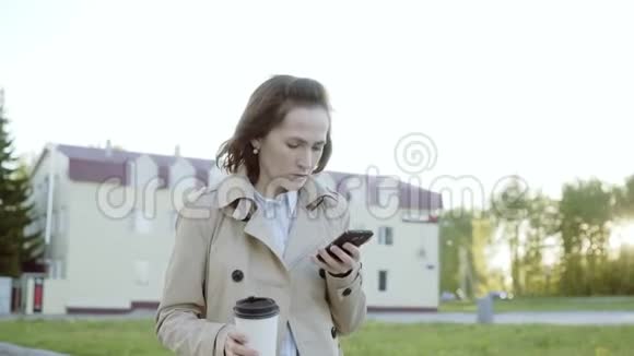 一位年轻漂亮的商业女学生在城市里走来走去喝着咖啡打着电话视频的预览图