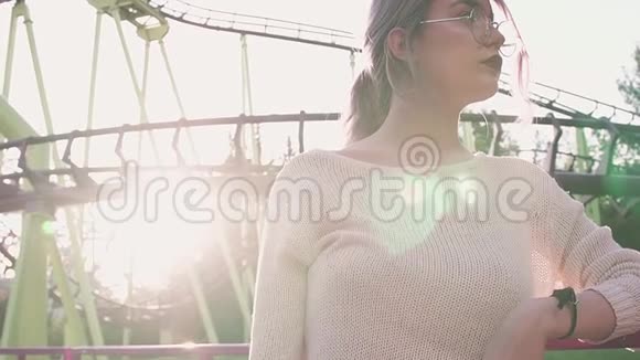 戴眼镜的漂亮女孩站在阳光下的过山车旁视频的预览图