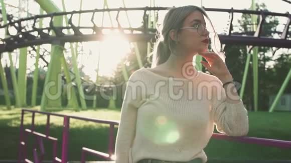 戴眼镜的漂亮女孩站在过山车旁阳光明媚视频的预览图