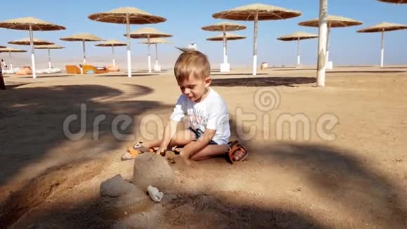 小男孩在海滩上建造沙堡的4k镜头视频的预览图
