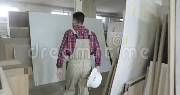 一个穿着工作服的年轻木匠在一家木工工厂的走廊里散步视频的预览图