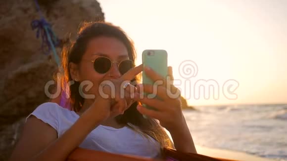 年轻的白种人潮女在海边的海滩上在美丽的金色夕阳下用吊床摆动视频的预览图