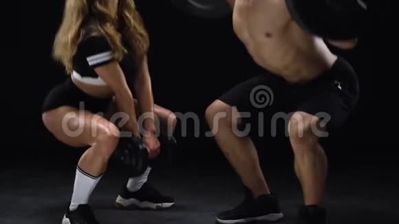运动的男人和女人蹲在额外的重量训练他们的腿和臀部在一个黑色的背景在工作室视频的预览图