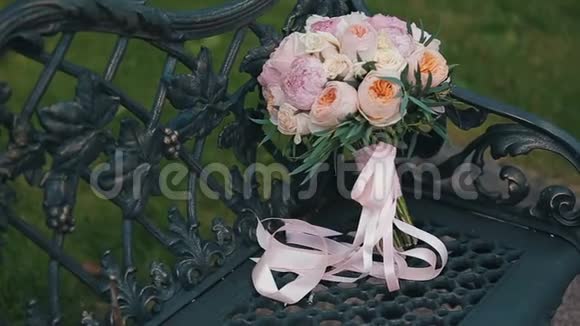 婚礼花束玫瑰和牡丹花在老式的黑色金属长凳上装饰着金属葡萄藤新娘视频的预览图
