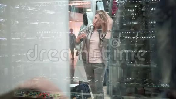 漂亮的女孩在商店里试穿一件时髦的夹克购物从窗口观看视频的预览图
