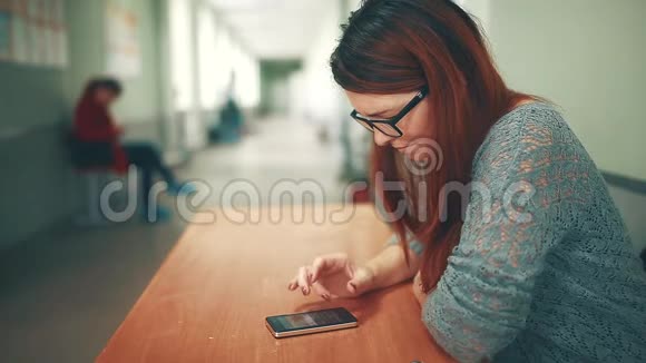 女大学生在大学学院的智能手机上看作业时做笔记坐着的女人视频的预览图