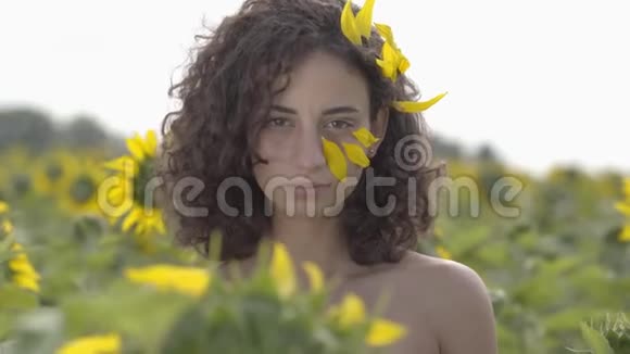 可爱的卷曲嬉戏的女孩看着镜头微笑地站在向日葵领域的肖像明亮的黄色视频的预览图