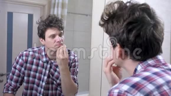 一个穿着格子衬衫的人在浴室里刮胡子看着镜子视频的预览图