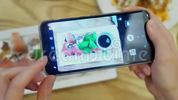 特写镜头女手在餐馆的智能手机上拍寿司视频的预览图