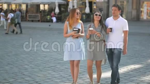 三个朋友在夏季温暖的日子里喝咖啡和在城市里散步两个戴太阳镜的女孩视频的预览图