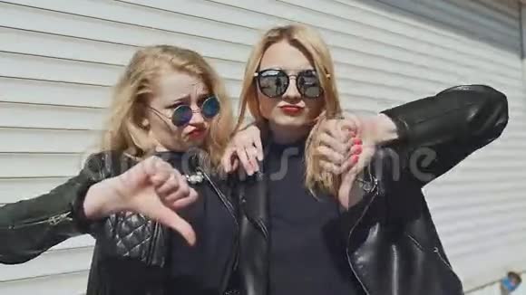 两个穿着皮夹克和白色背景太阳镜的时髦年轻女孩展示了一个手势手指朝下背景视频的预览图