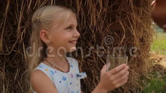 漂亮的金发女孩在农场的夏天在干草堆上喝着一杯新鲜牛奶视频的预览图