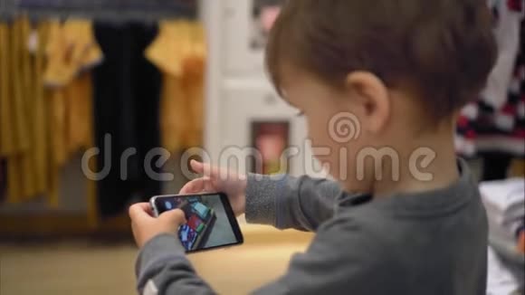 一个小男孩在商店里挑选衣服在智能手机上给她拍照视频的预览图