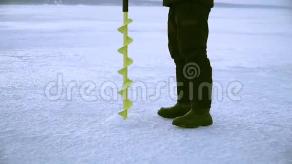一个渔民在冬天用冰钻在结冰的河上钻洞视频的预览图