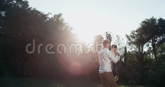 年轻的父亲在空气中抚养孩子头顶着大自然爸爸和儿子在夏天在公园户外玩耍日落时分视频的预览图