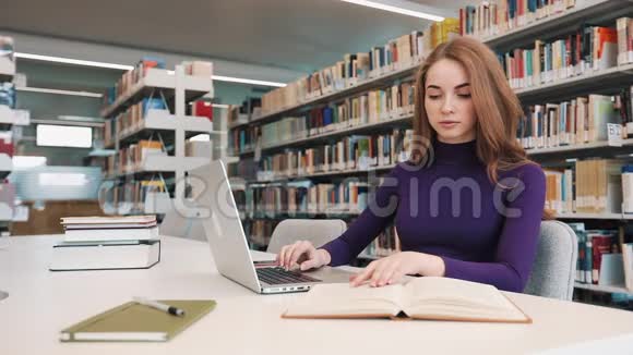 女学生拿着书和笔记本电脑坐在图书馆的桌子旁视频的预览图