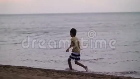 快乐的小男孩跑步玩得开心晚上在海滩上海浪跳跃童年假期视频的预览图