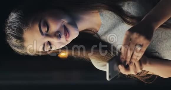 垂直视频年轻迷人的女人在夜城的街道上使用手机妇女使用手机经商视频的预览图