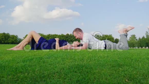 一个年轻的家庭正在等待一个孩子一个男人亲吻他怀孕的妻子一起躺在公园的草地上视频的预览图