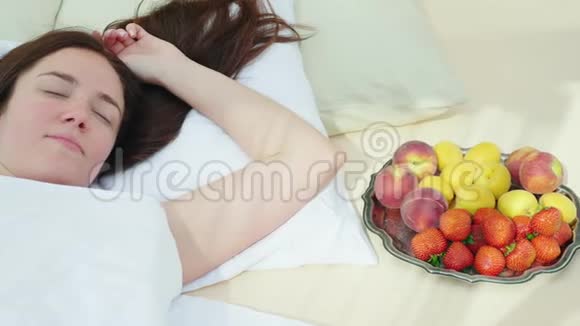 一个年轻的女人睡在一盘水果旁边床和早餐浪漫和蜜月浪漫视频的预览图