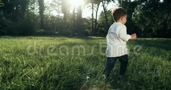可爱的小男孩穿着白衬衫在草地上奔跑动作缓慢4k婴儿后面的照相机视频的预览图