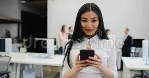 在与同事交流新想法时一位使用手机的亚洲女商人站在办公室视频的预览图
