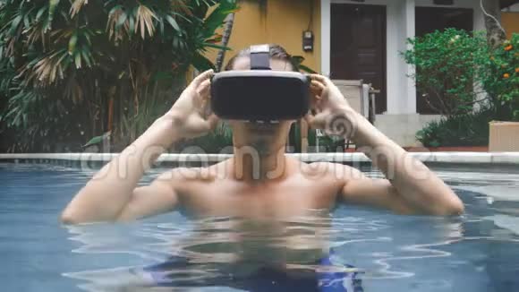 年轻人在游泳池游泳时使用虚拟现实眼镜在夏天使用虚拟现实耳机的经验视频的预览图